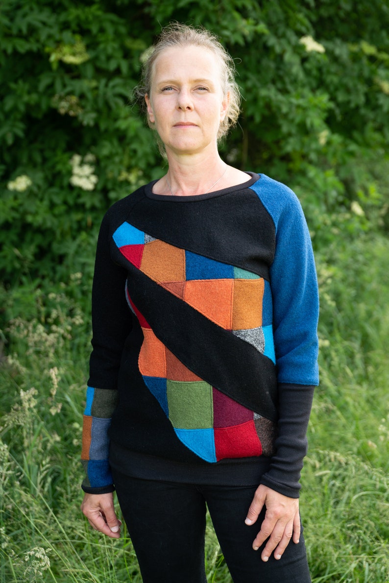 May include: A black sweater with a colourful patchwork design on the front. The sweater has long sleeves and a crew neck.