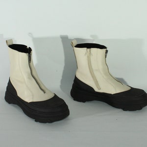 May include: A pair of white leather ankle boots with black rubber soles and a zipper up the front.