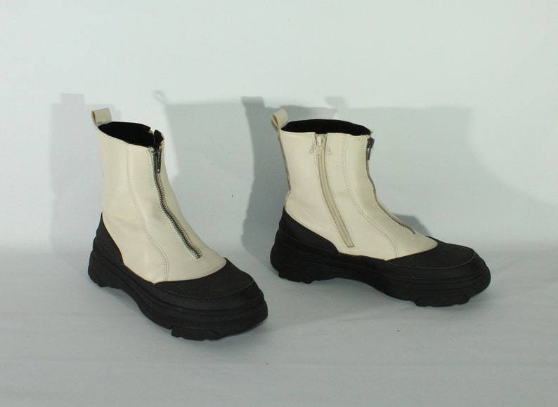 May include: A pair of white leather ankle boots with black rubber soles and a zipper up the front.