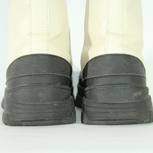 May include: A pair of white leather boots with black rubber soles. The boots have a chunky, platform-style sole.