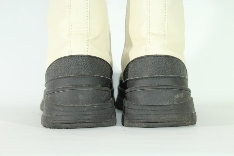 May include: A pair of white leather boots with black rubber soles. The boots have a chunky, platform-style sole.