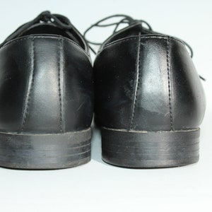 May include: A pair of black leather dress shoes with laces. The shoes are viewed from the back, showing the heels and the back of the shoes.
