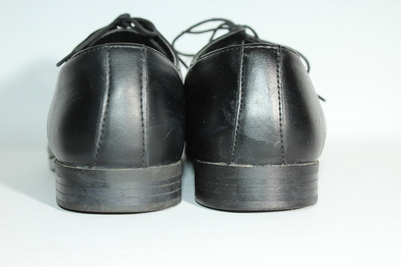 May include: A pair of black leather dress shoes with laces. The shoes are viewed from the back, showing the heels and the back of the shoes.