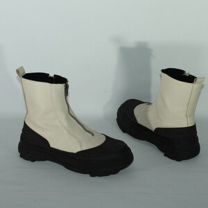 May include: A pair of white leather ankle boots with black rubber soles and a zipper up the front.