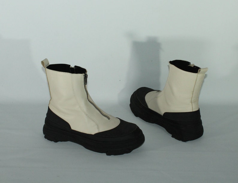 May include: A pair of white leather ankle boots with black rubber soles and a zipper up the front.