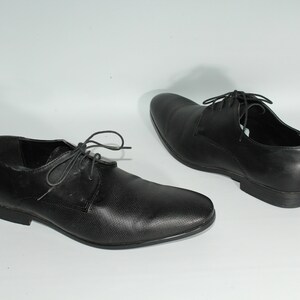 May include: A pair of black leather lace-up shoes with a textured pattern. The shoes have a pointed toe and a low heel.