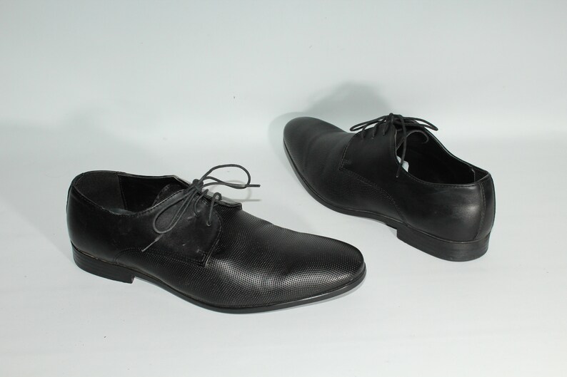 May include: A pair of black leather lace-up shoes with a textured pattern. The shoes have a pointed toe and a low heel.