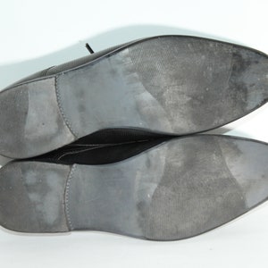 May include: A pair of black leather dress shoes with a textured sole. The shoes are shown from the bottom, with the soles facing the camera.