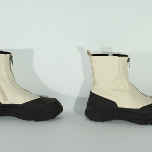May include: A pair of white ankle boots with black rubber soles and a zipper up the back.