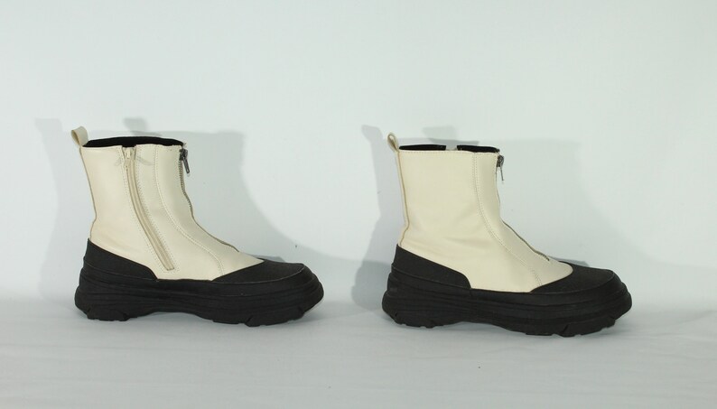 May include: A pair of white ankle boots with black rubber soles and a zipper up the back.