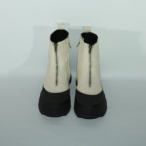 May include: A pair of white leather ankle boots with black rubber soles and a zipper up the front of each boot.