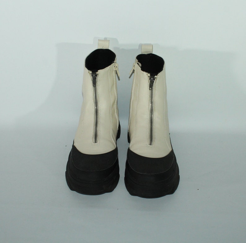 May include: A pair of white leather ankle boots with black rubber soles and a zipper up the front of each boot.