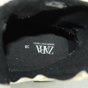 May include: Close-up of the inside of a black shoe with a white insole. The insole has the text "ZARA" and "MEMORY EFFECT INSOLE" printed on it. The shoe size is 38.