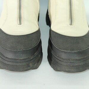 May include: A pair of white leather boots with black rubber soles and a zipper up the back.