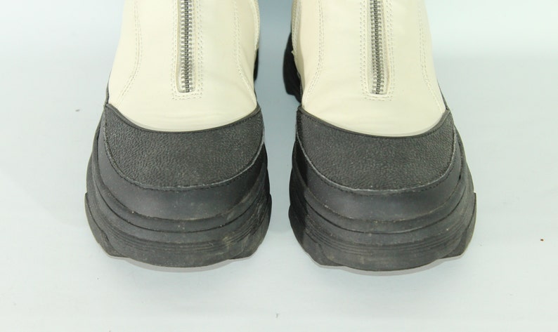 May include: A pair of white leather boots with black rubber soles and a zipper up the back.