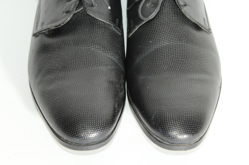 May include: A pair of black leather dress shoes with a textured pattern. The shoes have a lace-up closure and a pointed toe.