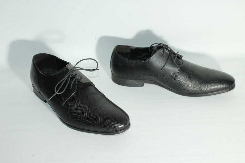 May include: A pair of black leather lace-up shoes with a textured pattern.