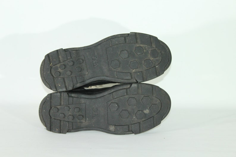 May include: Close-up of the black soles of a pair of shoes. The soles have a textured pattern with hexagonal shapes and the word "ZARA" is visible on the soles.