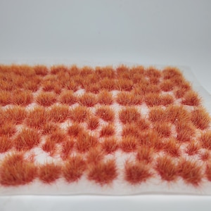 May include: A sheet of orange-brown static grass tufts, arranged in rows on a white background. The tufts are made of fine, synthetic fibers and are designed for use in model railroading or other hobby projects.