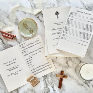 May include: A wedding ceremony program booklet with a white background and black text. The booklet includes the order of service, the names of the bride and groom, and the names of the wedding party. The booklet is open to the page with the order of service. The booklet is lying on a white marble surface.
