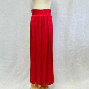 May include: A vibrant red, floor-length skirt with a high waist and pleats. The skirt is made of a soft, flowing fabric and is displayed on a mannequin. The skirt's bold color and classic design make it a versatile wardrobe piece.