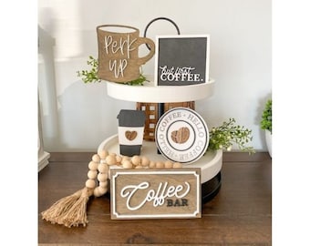 May include: A two-tiered wooden tray with coffee-themed decorations. Includes a mug that says "Perk Up", a sign that says "But first, coffee", a coffee cup, a coaster, and a sign that says "Coffee Bar".