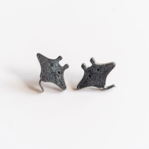 May include: A pair of silver-colored earrings shaped like manta rays. The earrings have a sparkly finish.