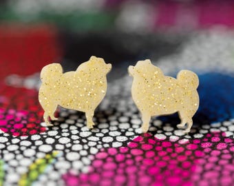 May include: A pair of gold glitter dog silhouette earrings. The earrings are made of a white material and have a sparkly gold finish.