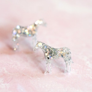 May include: Two silver glitter horse figurines on a pink background.