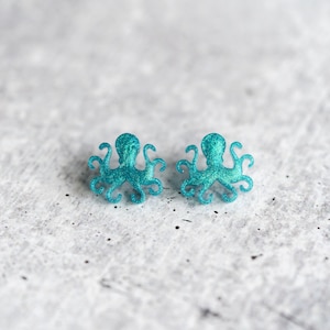 May include: A pair of turquoise glitter octopus earrings. The earrings are made of a sparkly material and are shaped like octopuses.