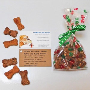 May include: A bag of dog treats tied with a green and white ribbon. The bag is filled with peanut butter and maple biscuits. The bag is labeled "terWOOFic Bacon, Peanut Butter and Maple Biscuits". The label also lists the ingredients: whole wheat flour, natural peanut butter, bacon, bacon drippings, all natural maple syrup and honey blend, egg. The label also says "These freeze well!" and includes the website address "www.terwoofic.com".