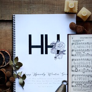 以下が含まれることがあります： HHの文字と花のデザインが描かれた白黒の画像。下のテキストには「Happy Hymnedy Winter Guide」と「of the Father's love begotten, all the way my Savior leads, more is love vast as the ocean, by April Brauer」と書いてあります。
