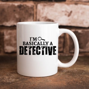 May include: White ceramic mug with a black graphic that says "I'm basically a detective" with a magnifying glass icon.