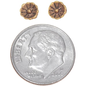May include: Two gold-colored flower-shaped earrings with a smaller gold-colored circle in the center. The earrings are shown next to a US dime for size comparison.