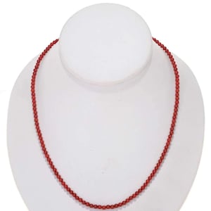 May include: A red coral bead necklace on a white display stand.