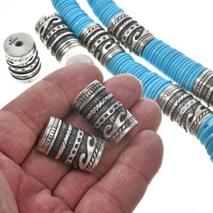 May include: A turquoise and silver necklace with decorative silver beads. The beads have a geometric pattern and are made of sterling silver.