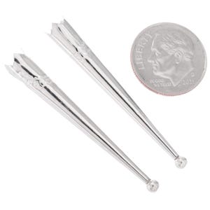 May include: Two silver-colored collar stays with decorative tops and rounded tips. A US dime coin is next to the collar stays for size comparison. The collar stays are made of a shiny metal.