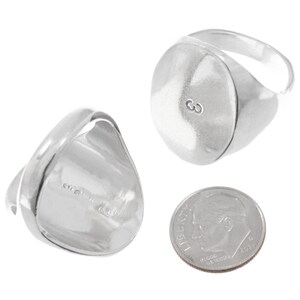 May include: A set of two silver signet rings. One ring features a smooth, oval face with the letter "G" engraved. The other ring is shown from the side, displaying the band and the back of the oval face. A dime is included for size reference.