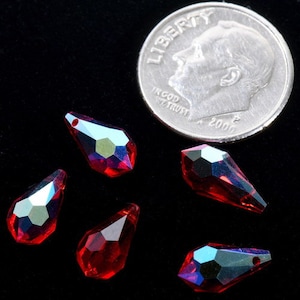 May include: Five red teardrop-shaped crystal beads with iridescent accents. The beads are approximately the size of a UK ten pence coin.