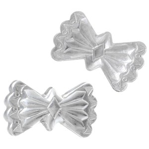 May include: Two silver-coloured bow-tie shaped ornaments. Each ornament has a central diamond shape and radiating lines, with a scalloped edge. The ornaments are displayed against a white background.