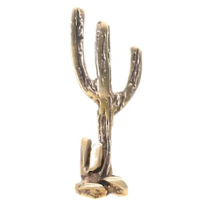 May include: A gold-colored metal cactus sculpture with a textured surface. The cactus has three arms and a small base.