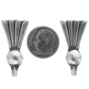May include: Two silver-toned furniture feet with a fan-like design, each with a rounded base and a tapered bottom. A U.S. dime is placed between them for size comparison. The dime shows the profile of a man and the words "Liberty" and "In God We Trust".