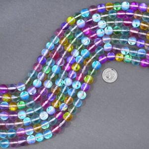 May include: A strand of iridescent glass beads in various colors, including blue, green, purple, and yellow. The beads are round and have a smooth, polished finish. The beads are arranged in a curved line, with a US quarter coin for scale.