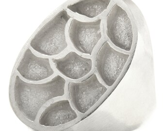 May include: A silver ring with a textured, oval-shaped design. The design features a pattern of overlapping, semi-circular shapes.