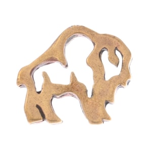 May include: A bronze-coloured metal bison pendant with an openwork design. The pendant features the silhouette of a bison, with details of the head, body, and legs. The metal has a slightly aged appearance, suggesting a vintage or rustic style.