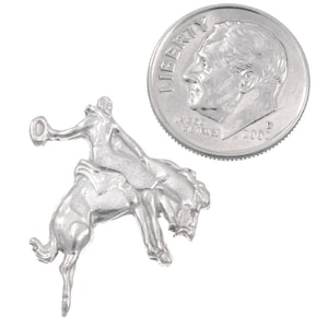 May include: Silver charm of a cowboy riding a bucking horse. The charm is about the size of a US dime.
