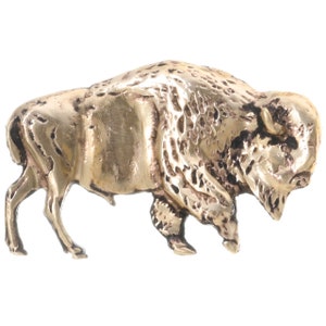 May include: A gold-coloured metal bison sculpture. The bison is standing with its head lowered and its horns visible. The sculpture is detailed with textured fur and a realistic appearance.