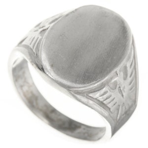May include: A silver signet ring with an oval shaped top and an eagle design on the sides.