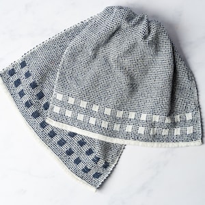 Puede incluir: Dos toallas de cocina azules y blancas con un patrón geométrico. Las toallas están dobladas y tienen un borde blanco.