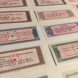 May include: A collection of vintage Chinese food ration coupons. The coupons are printed on paper and feature red and blue borders. The coupons are in denominations of 2 and 5. The coupons have Chinese text and a red star.